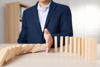 Photo of Man stopping wooden blocks from falling at table, closeup. Domino effect