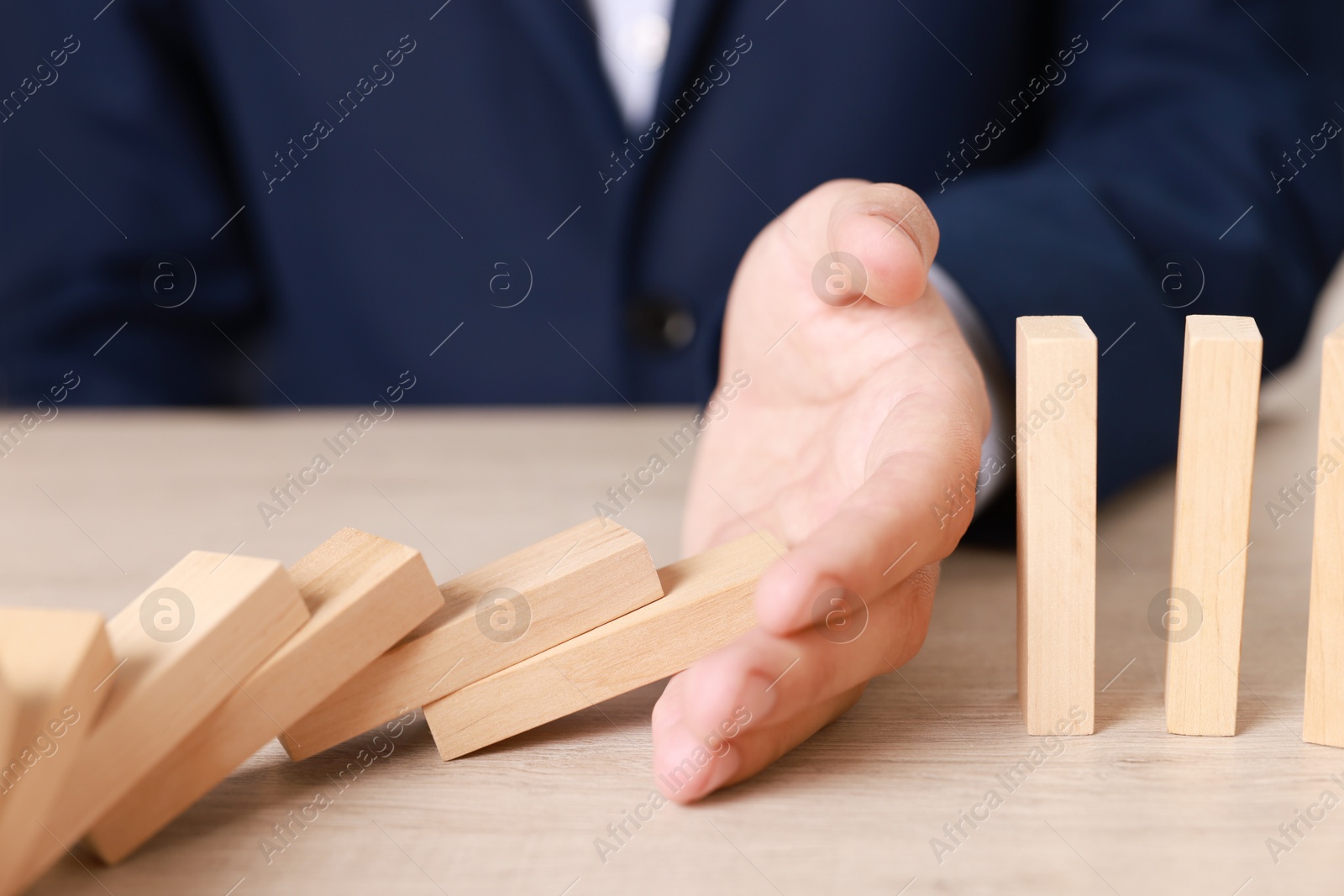 Photo of Man stopping wooden blocks from falling at table, closeup. Domino effect