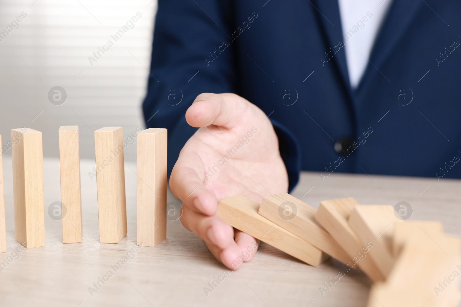 Photo of Man stopping wooden blocks from falling at table, closeup. Domino effect