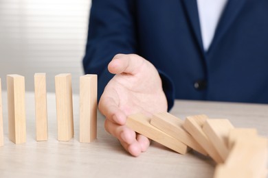 Photo of Man stopping wooden blocks from falling at table, closeup. Domino effect