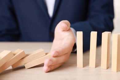 Photo of Man stopping wooden blocks from falling at table, closeup. Domino effect