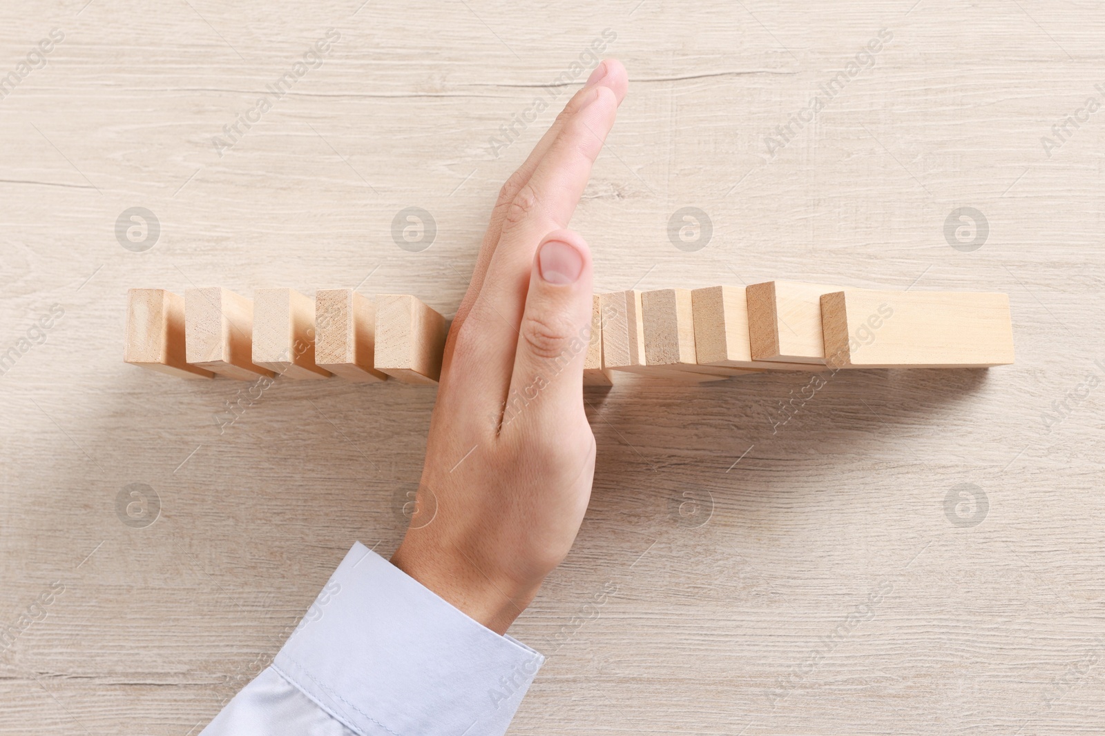 Photo of Man stopping wooden blocks from falling at table, top view. Domino effect