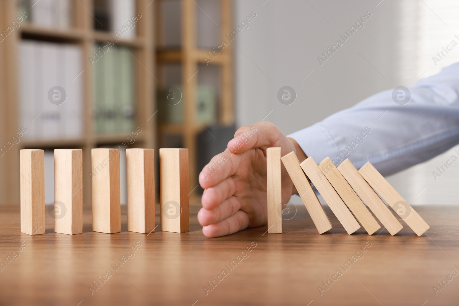 Photo of Man stopping wooden blocks from falling at table, closeup. Domino effect