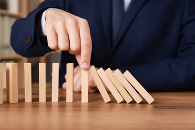 Photo of Man stopping wooden blocks from falling at table, closeup. Domino effect