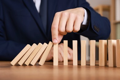 Photo of Man stopping wooden blocks from falling at table, closeup. Domino effect