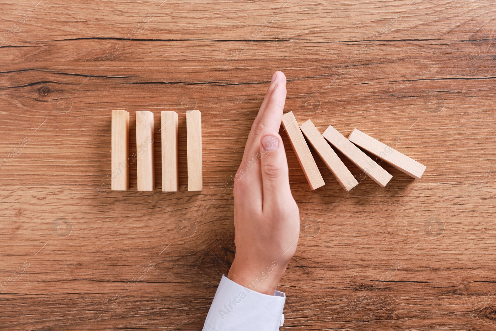 Photo of Man stopping wooden blocks from falling at table, top view. Domino effect