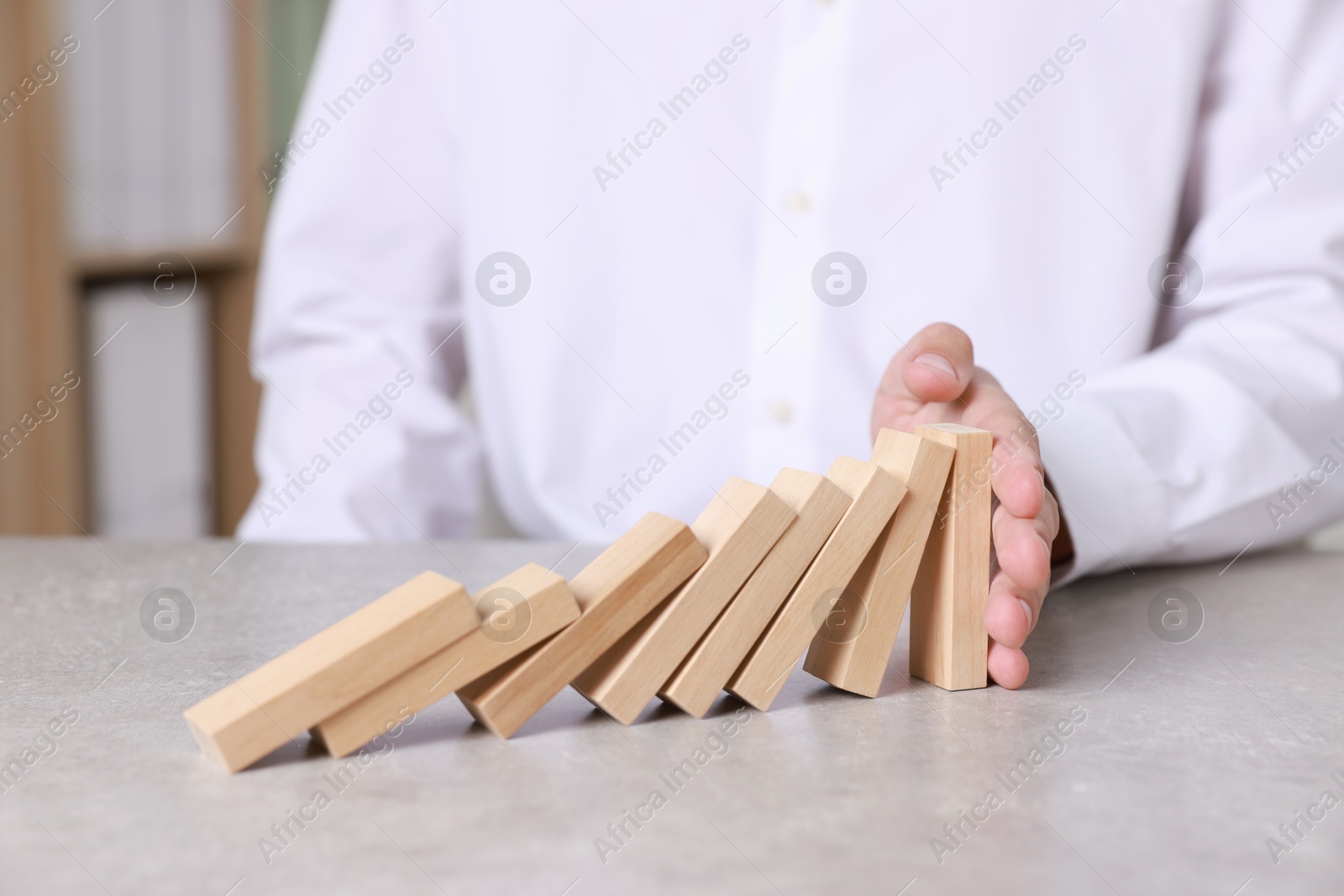 Photo of Man stopping wooden blocks from falling at table, closeup. Domino effect