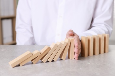 Photo of Man stopping wooden blocks from falling at table, closeup. Domino effect