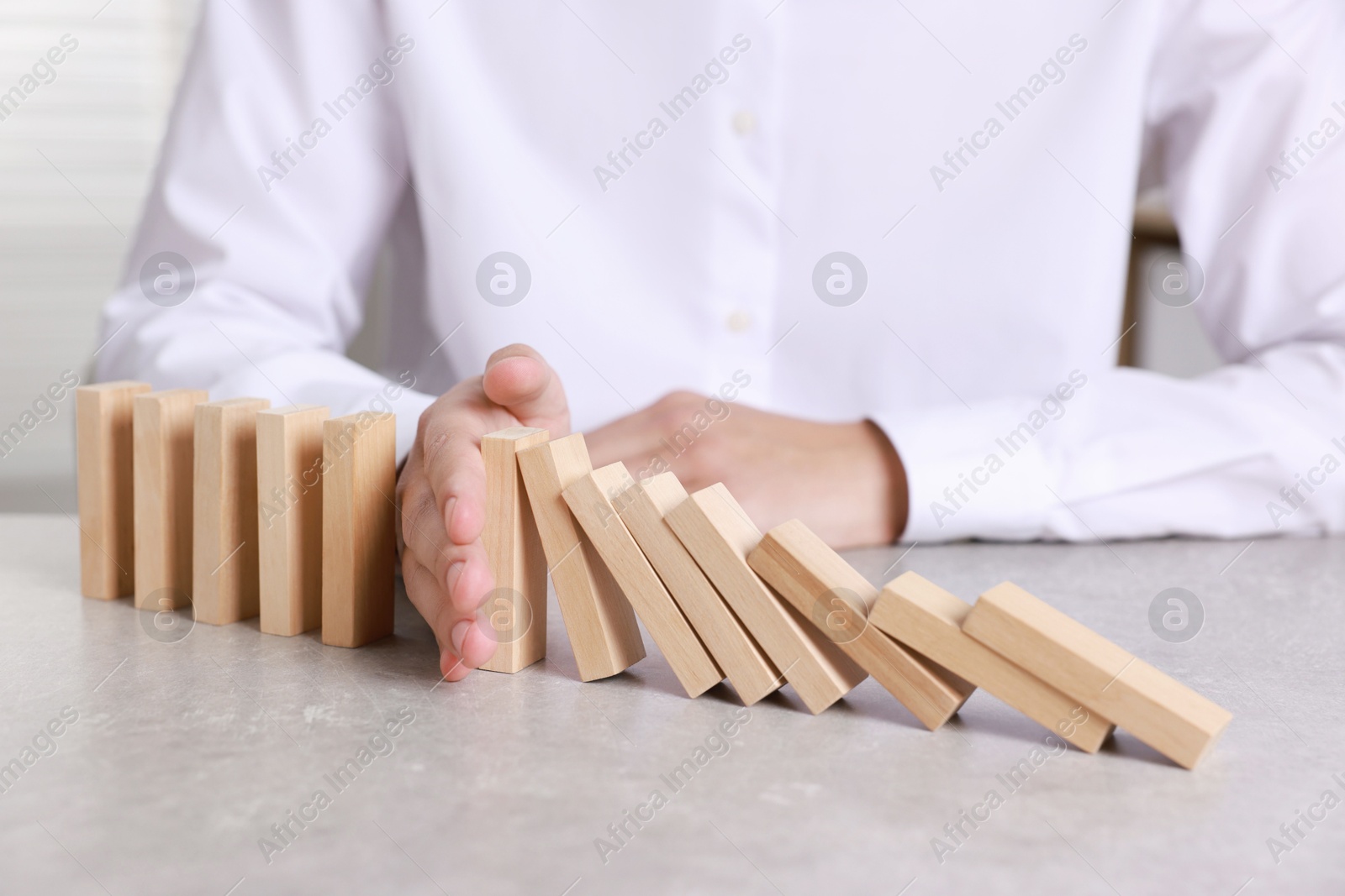 Photo of Man stopping wooden blocks from falling at table, closeup. Domino effect