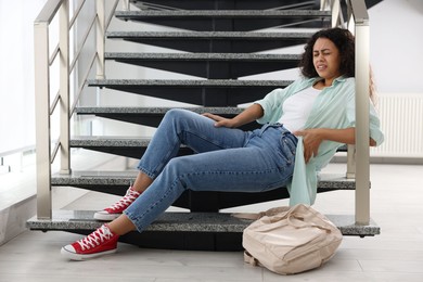 Photo of Woman with injured back on stairs in building after fall. Dangerous accident