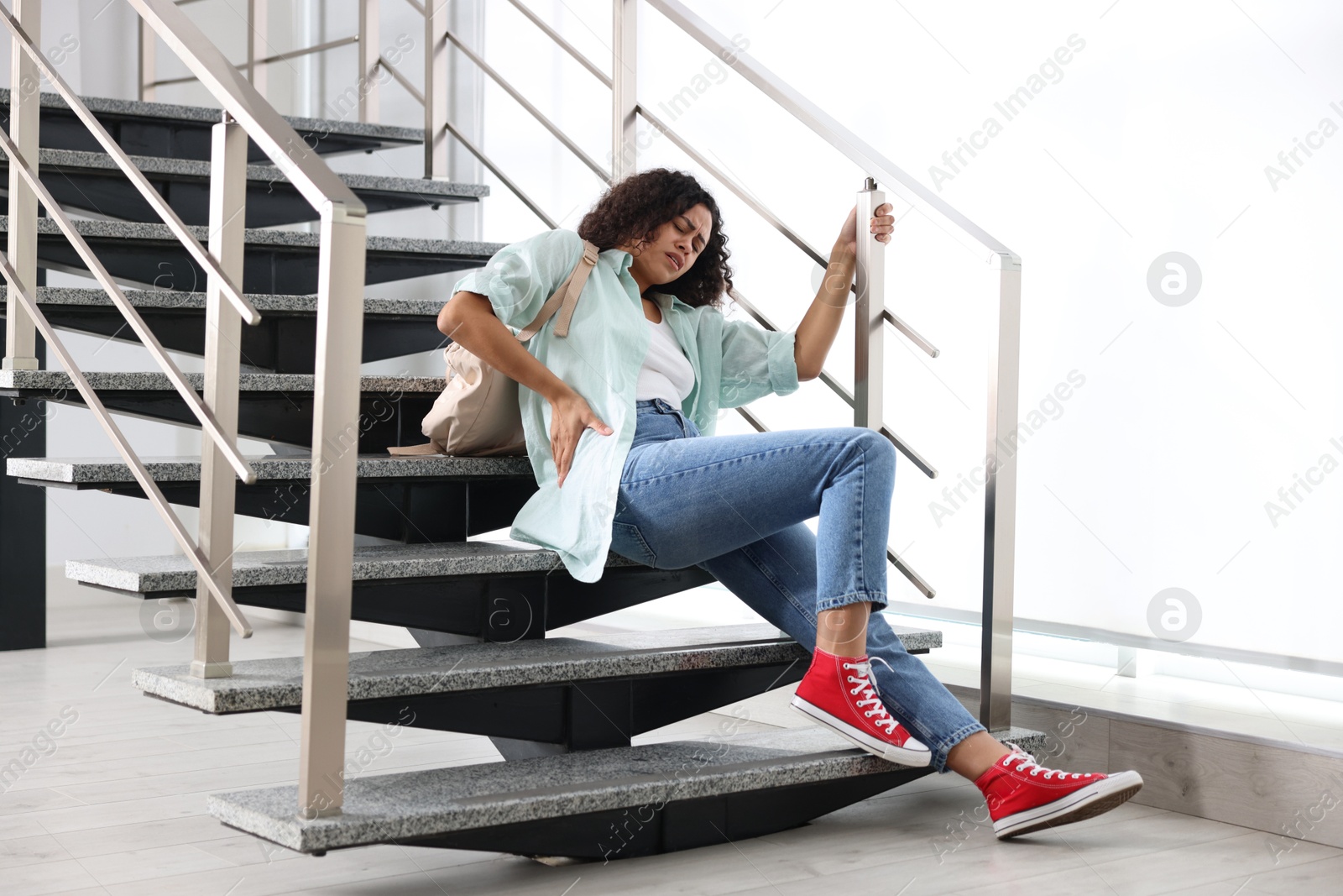 Photo of Woman with injured back on stairs in building after fall. Dangerous accident