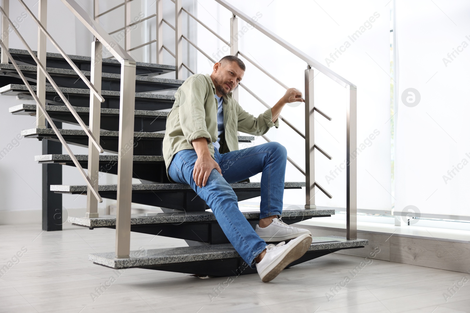 Photo of Man with injured leg on stairs in building after fall. Dangerous accident