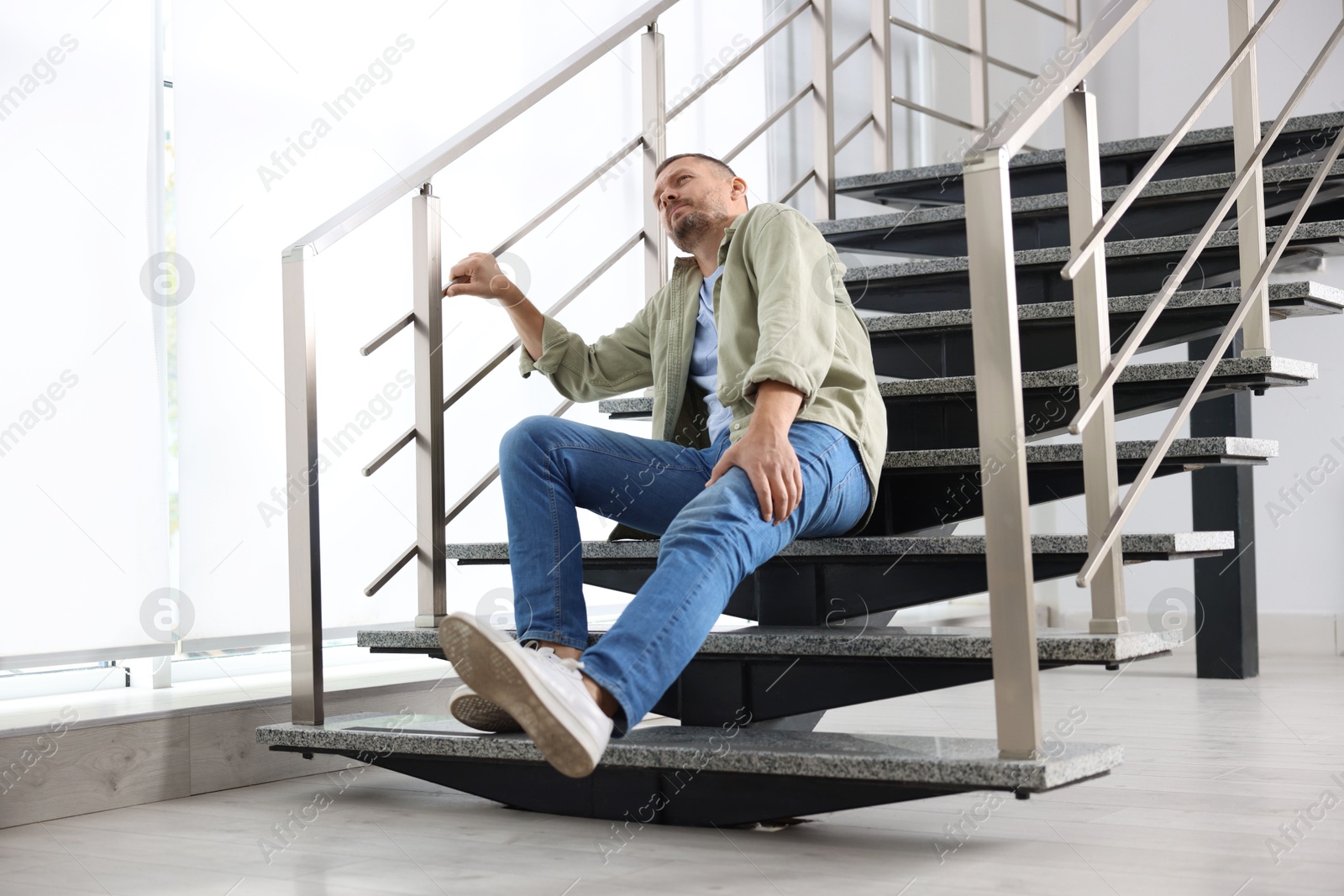 Photo of Man with injured leg on stairs in building after fall. Dangerous accident