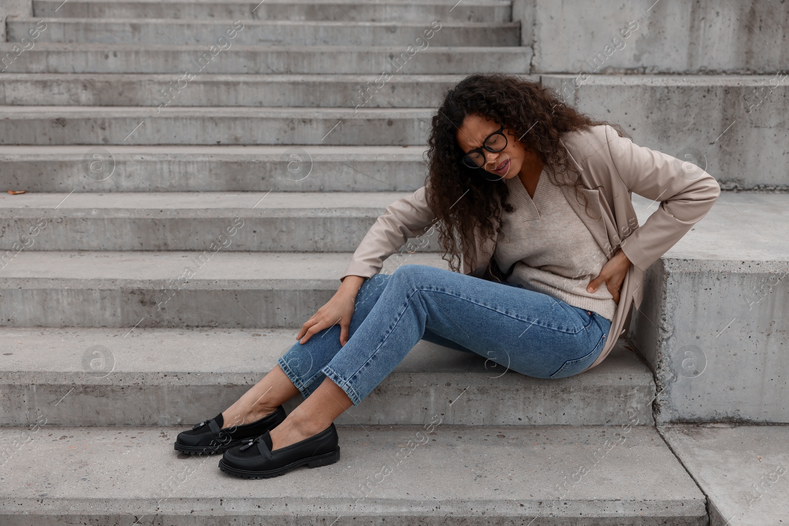 Photo of Woman with injured back on stairs outdoors after fall. Dangerous accident