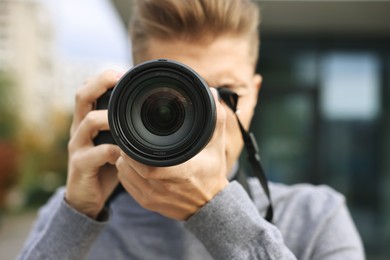 Photo of Professional photographer taking picture with camera outdoors, selective focus