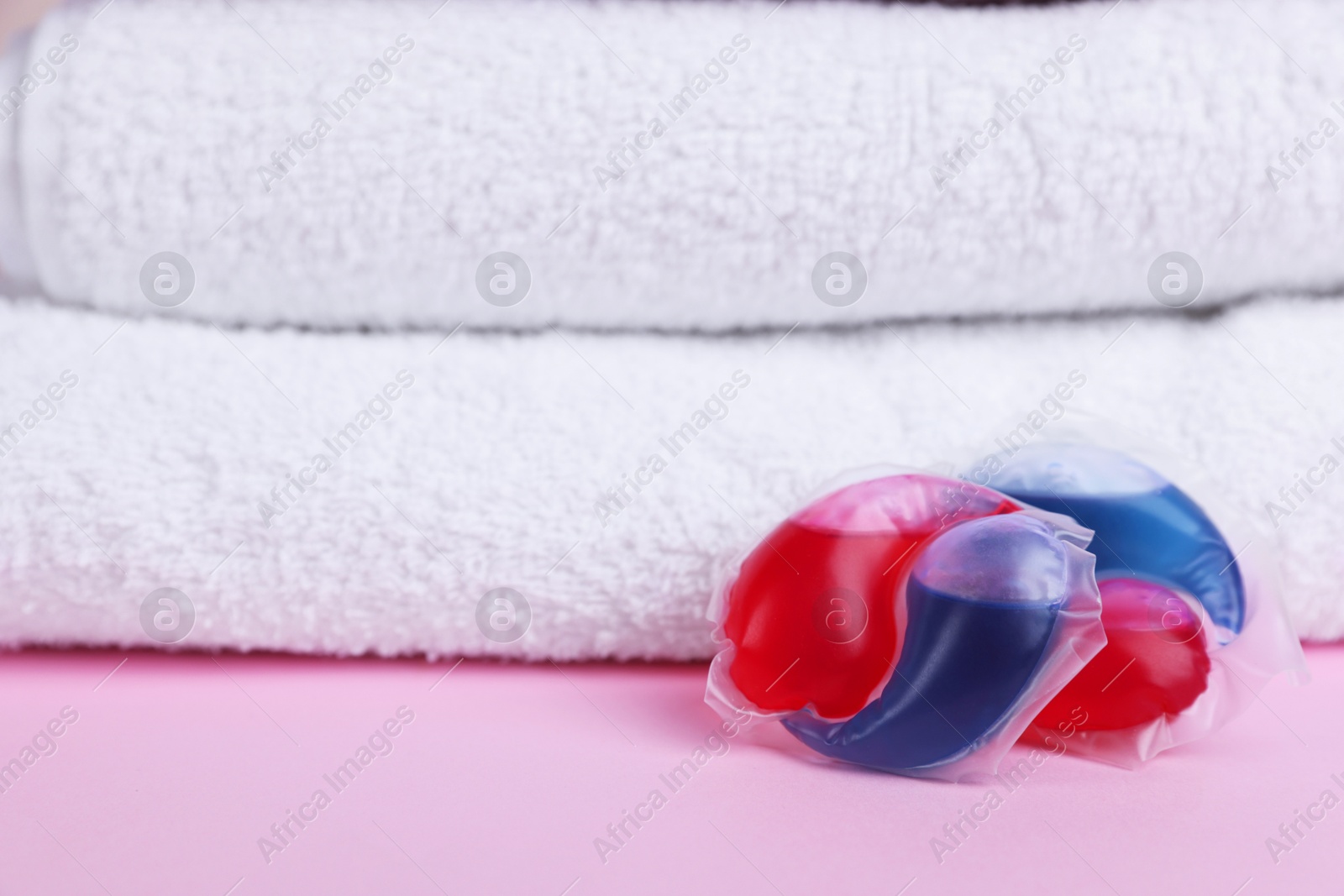 Photo of Laundry detergent capsules and clean towel on pink background, closeup