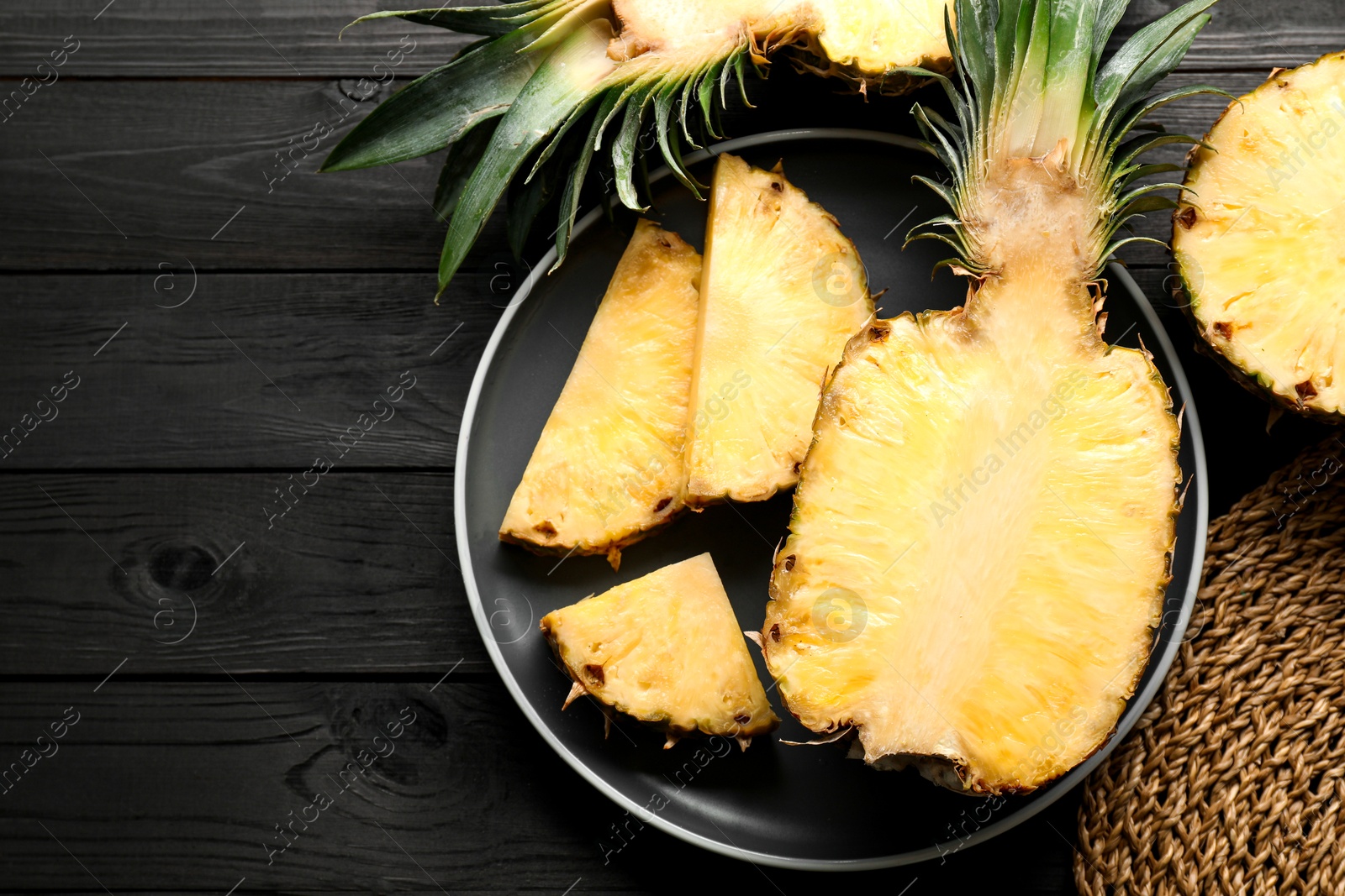 Photo of Cut fresh ripe pineapple on black wooden table, top view. Space for text