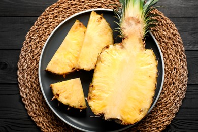 Photo of Cut fresh ripe pineapple on black wooden table, top view