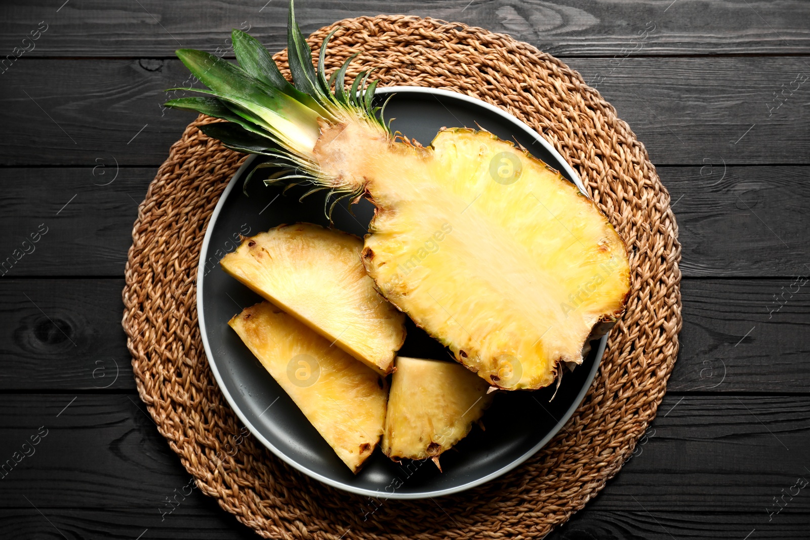 Photo of Cut fresh ripe pineapple on black wooden table, top view