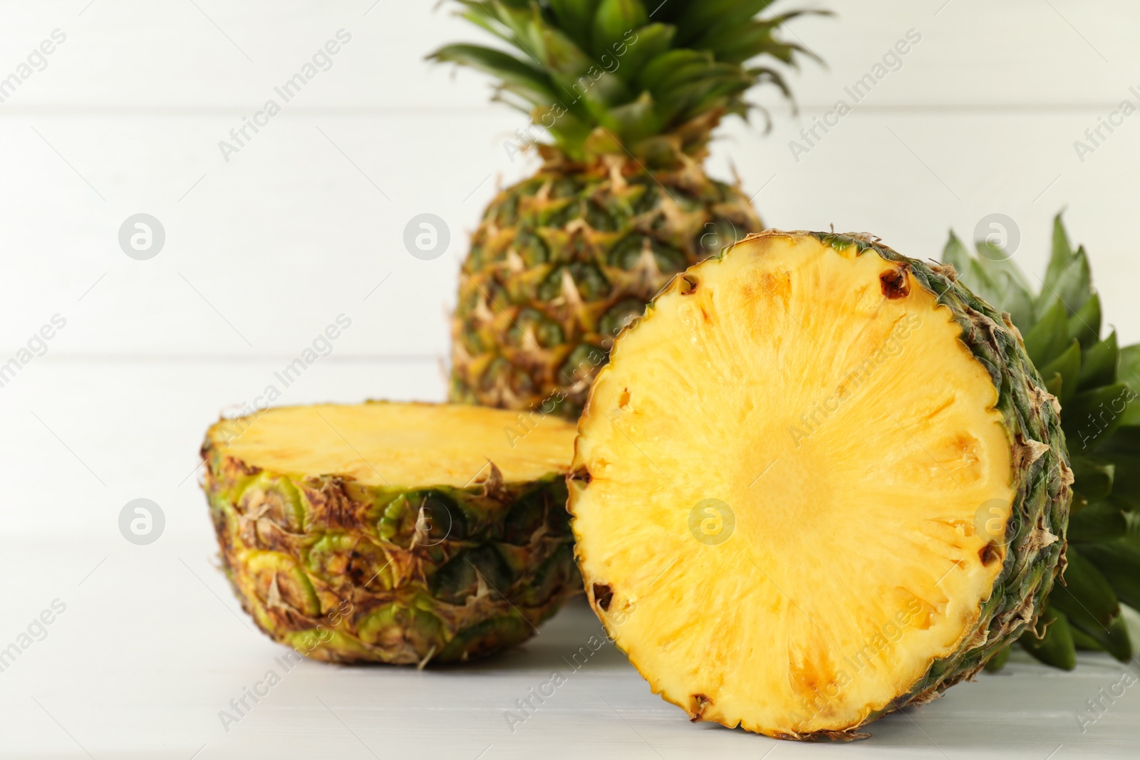 Photo of Whole and sliced fresh ripe pineapples on white wooden table