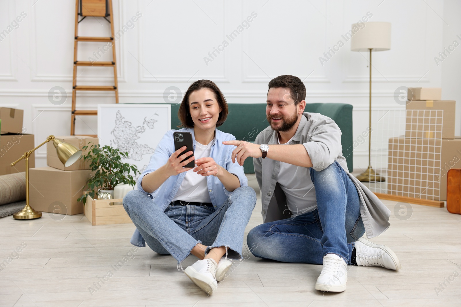 Photo of Moving day. Happy couple with smartphone in their new home