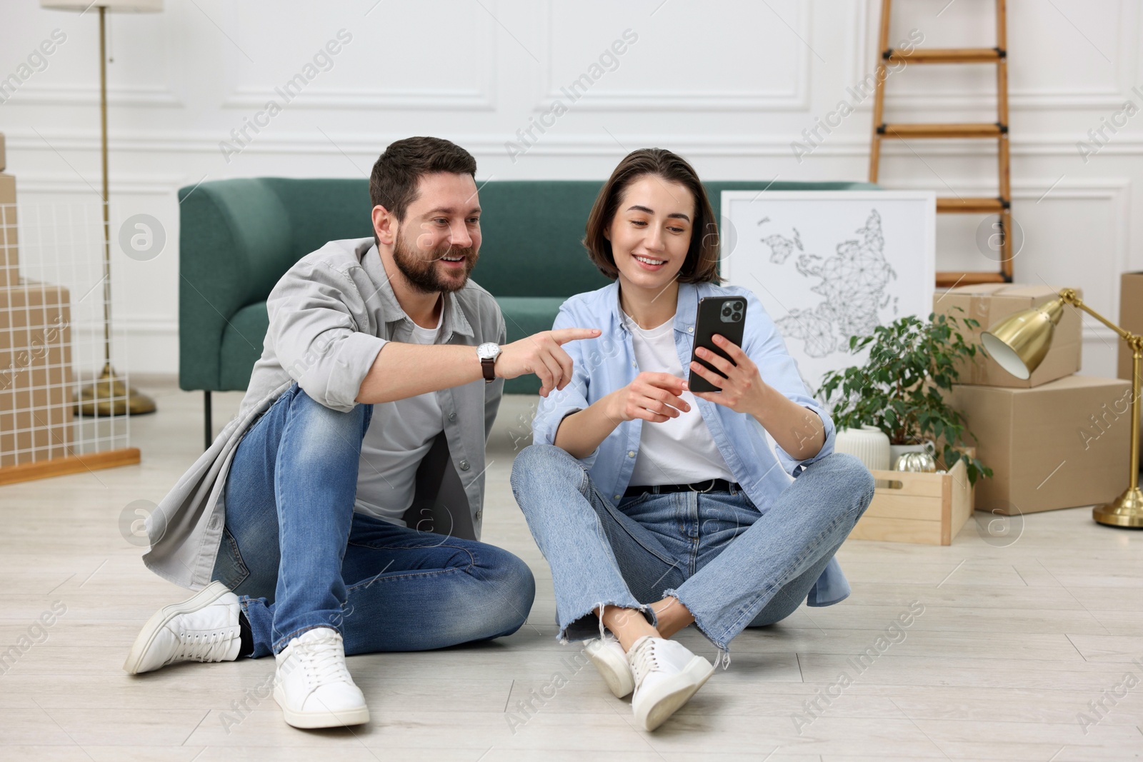 Photo of Moving day. Happy couple with smartphone in their new home