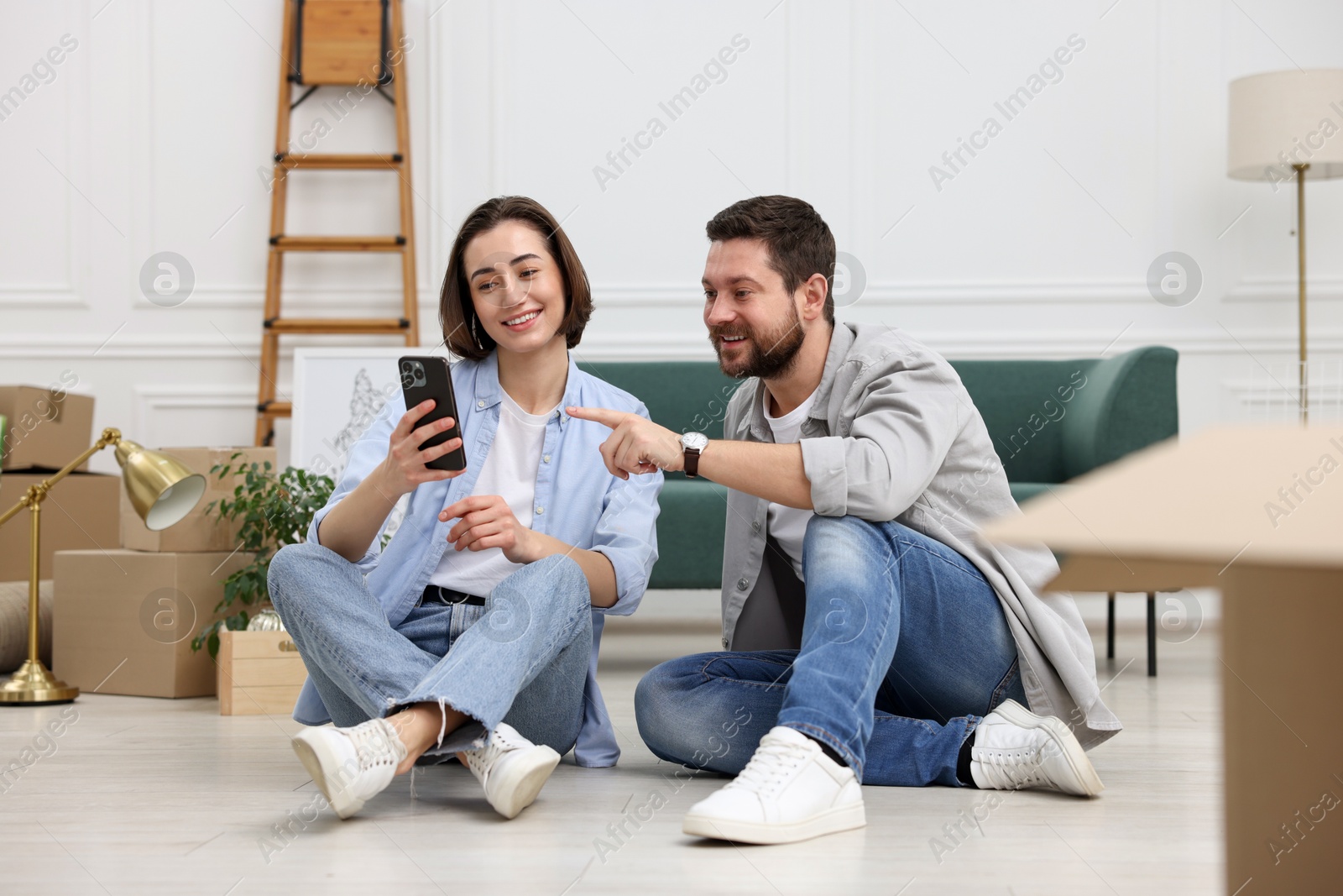 Photo of Moving day. Happy couple with smartphone in their new home