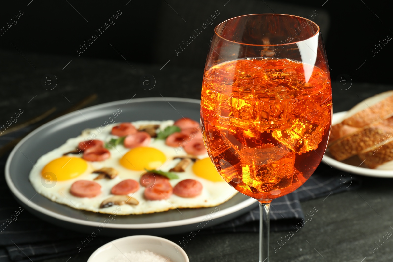 Photo of Tasty brunch. Aperol cocktail, delicious fried eggs with sausage served on black table, closeup