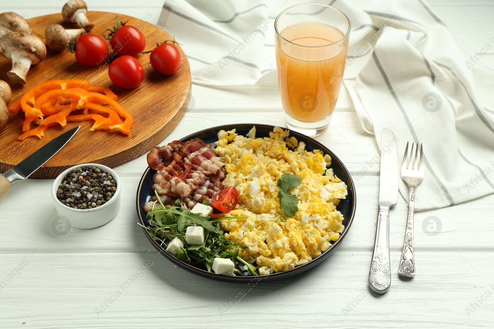 Photo of Tasty brunch. Delicious scrambled eggs, bacon, salad and glass of juice served on white wooden table