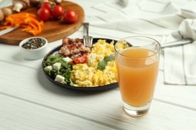 Photo of Tasty brunch. Glass of apple juice and scrambled eggs with bacon served on white wooden table, closeup