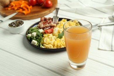 Photo of Tasty brunch. Glass of apple juice and scrambled eggs with bacon served on white wooden table, closeup