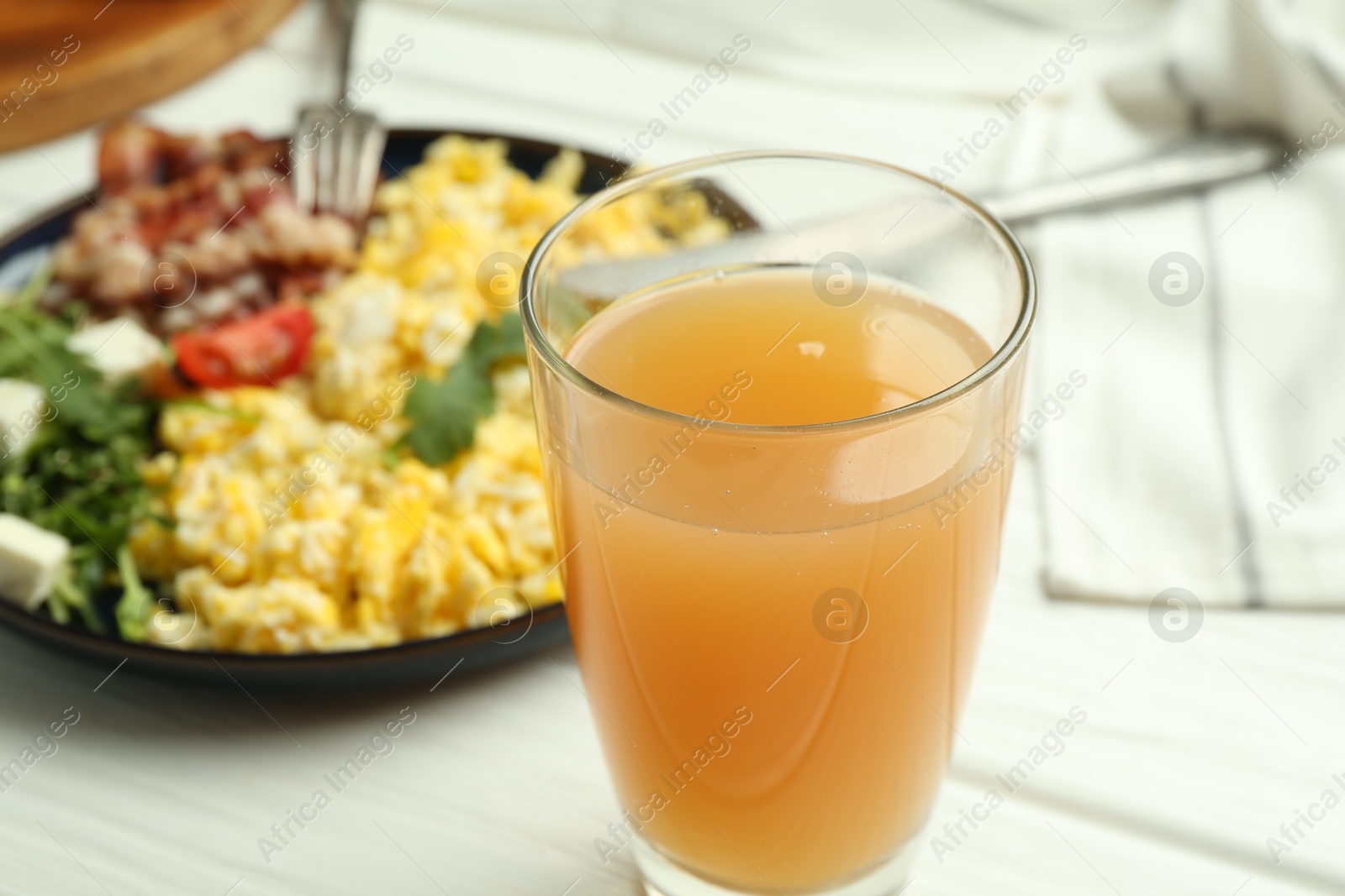 Photo of Tasty brunch. Glass of apple juice and scrambled eggs with bacon served on white wooden table, closeup