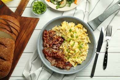 Photo of Tasty brunch. Delicious scrambled eggs, bacon and salad served on white wooden table, flat lay