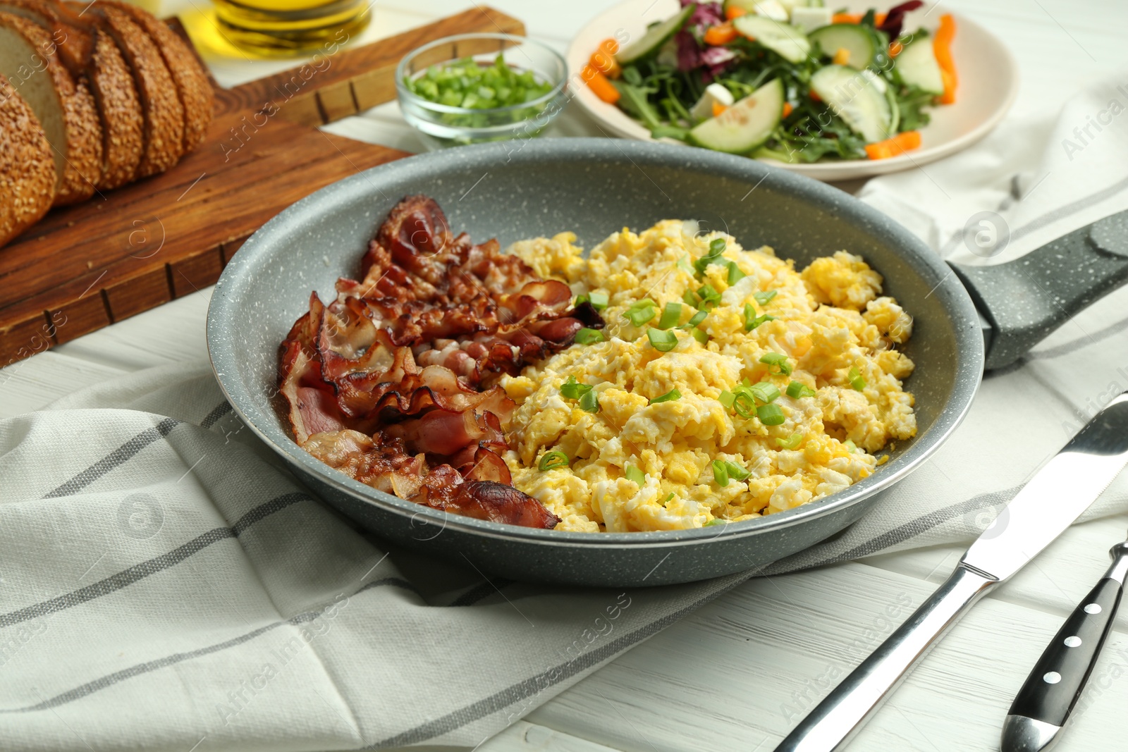 Photo of Tasty brunch. Delicious scrambled eggs, bacon and salad served on white wooden table, closeup