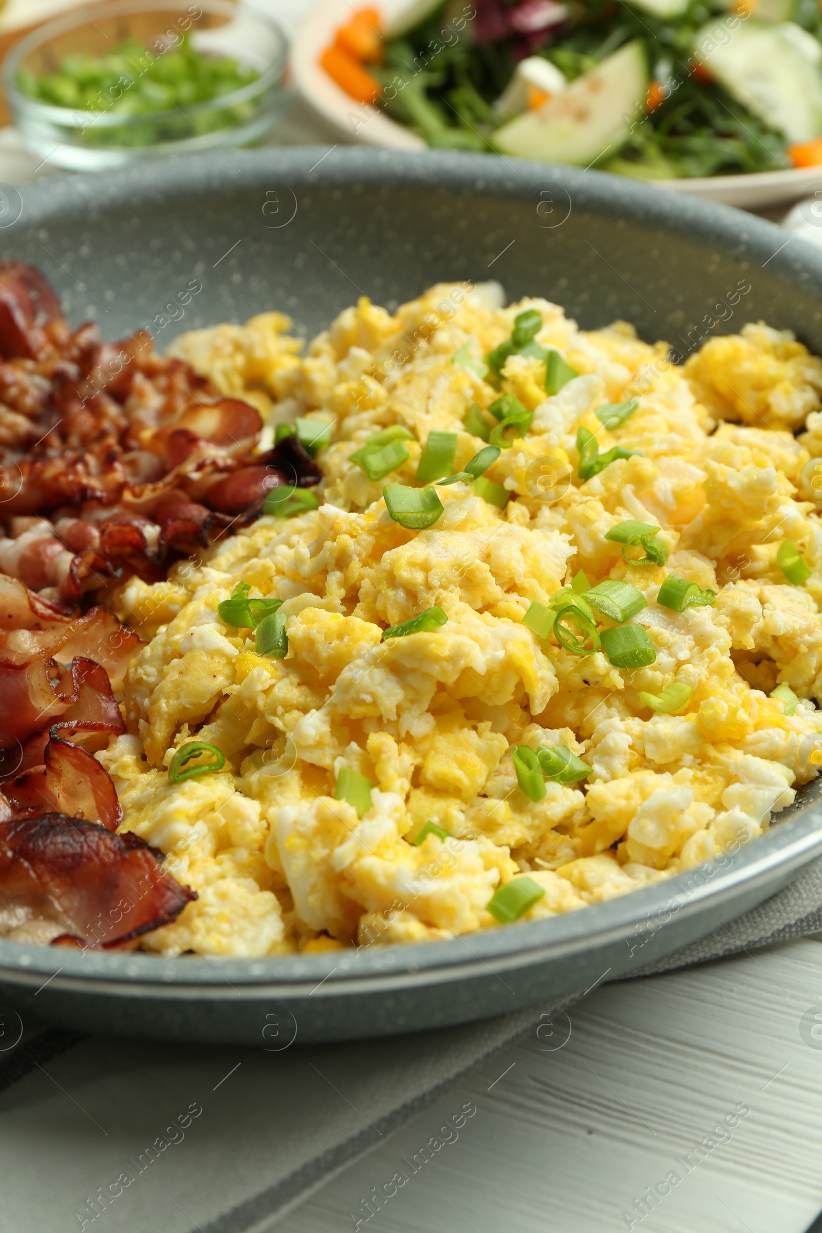 Photo of Tasty brunch. Delicious scrambled eggs, bacon and salad served on white wooden table, closeup