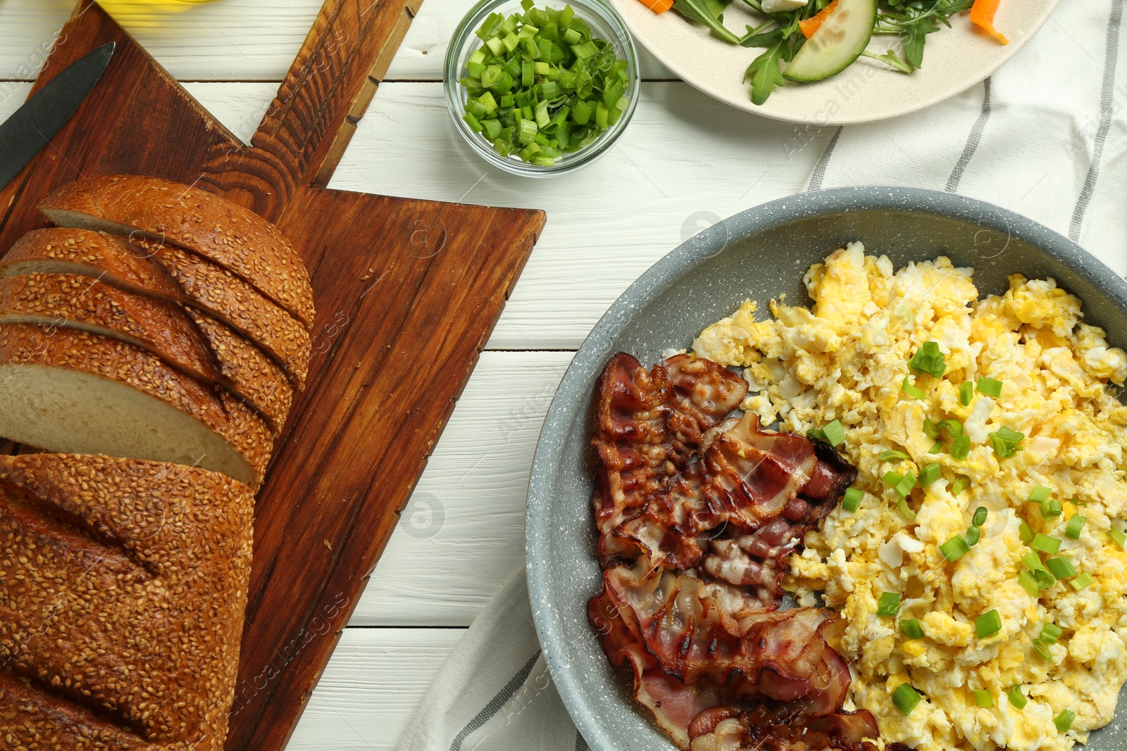 Photo of Tasty brunch. Delicious scrambled eggs, bacon and salad served on white wooden table, flat lay