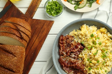 Photo of Tasty brunch. Delicious scrambled eggs, bacon and salad served on white wooden table, flat lay