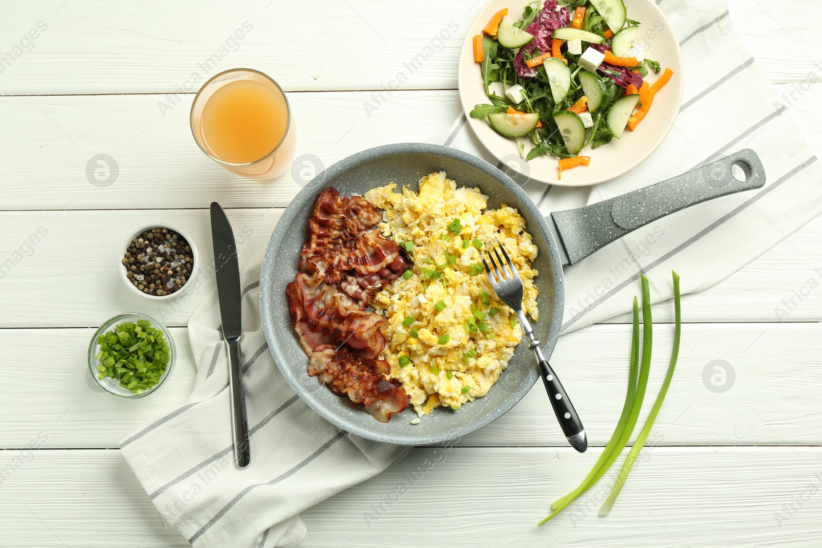 Photo of Tasty brunch. Delicious scrambled eggs, bacon, salad and glass of juice served on white wooden table, flat lay