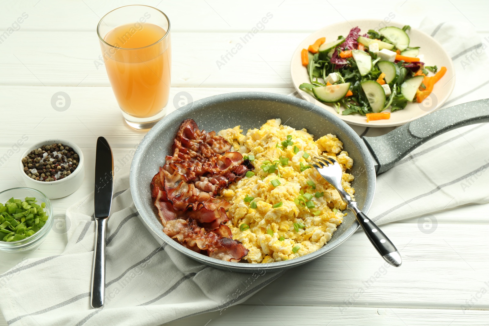 Photo of Tasty brunch. Delicious scrambled eggs, bacon, salad and glass of juice served on white wooden table