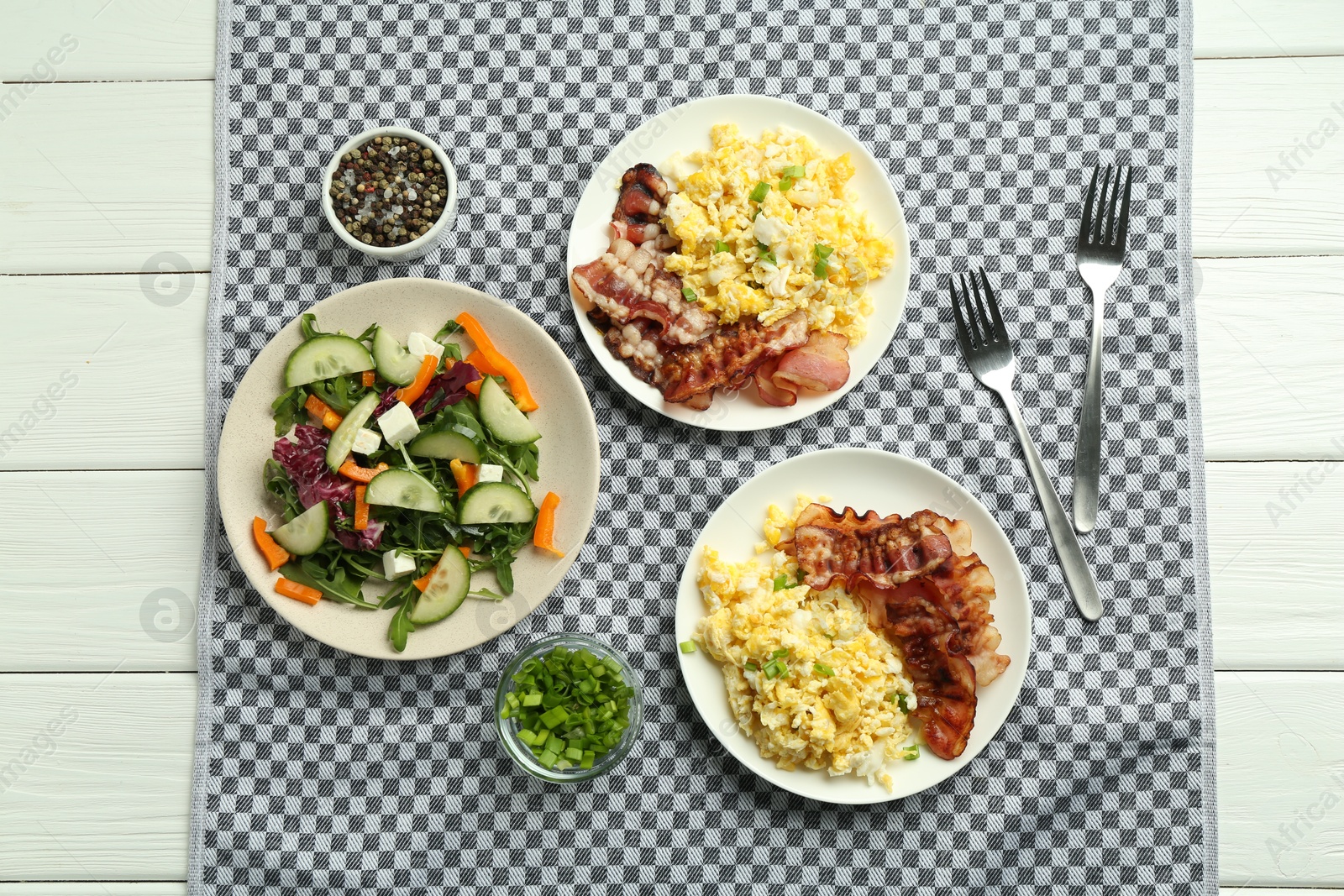 Photo of Tasty brunch. Delicious scrambled eggs, bacon and salad served on white wooden table, flat lay