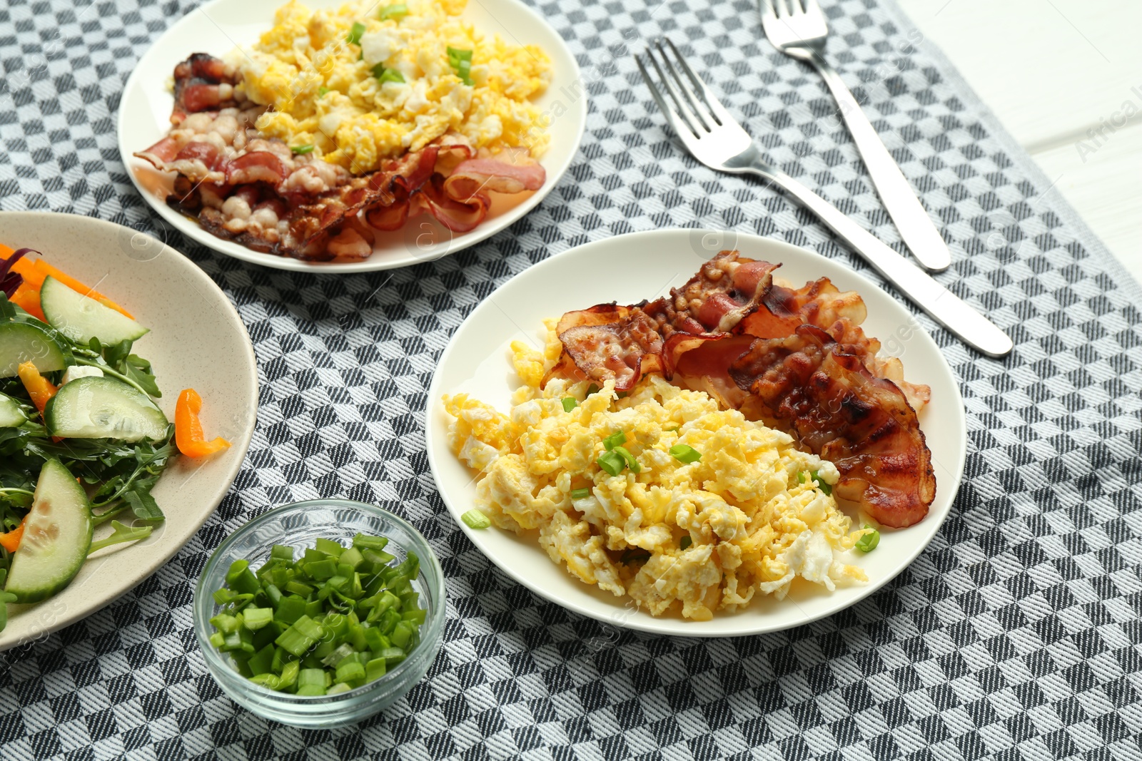 Photo of Tasty brunch. Delicious scrambled eggs, bacon and salad served on white table