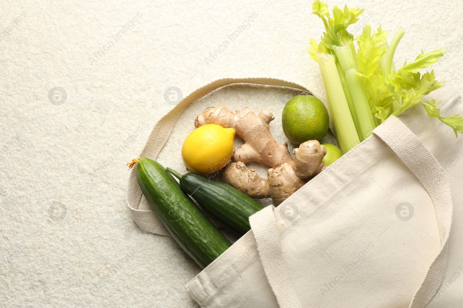 Photo of Eco bag with vegetables, fruits and ginger on white textured table, top view. Space for text