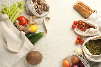 Photo of Eco bags with different food products on white textured table, flat lay. Space for text