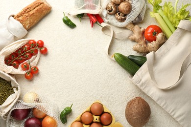 Photo of Eco bags with different food products on white textured table, flat lay. Space for text