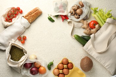 Photo of Eco bags with different food products on white textured table, flat lay. Space for text