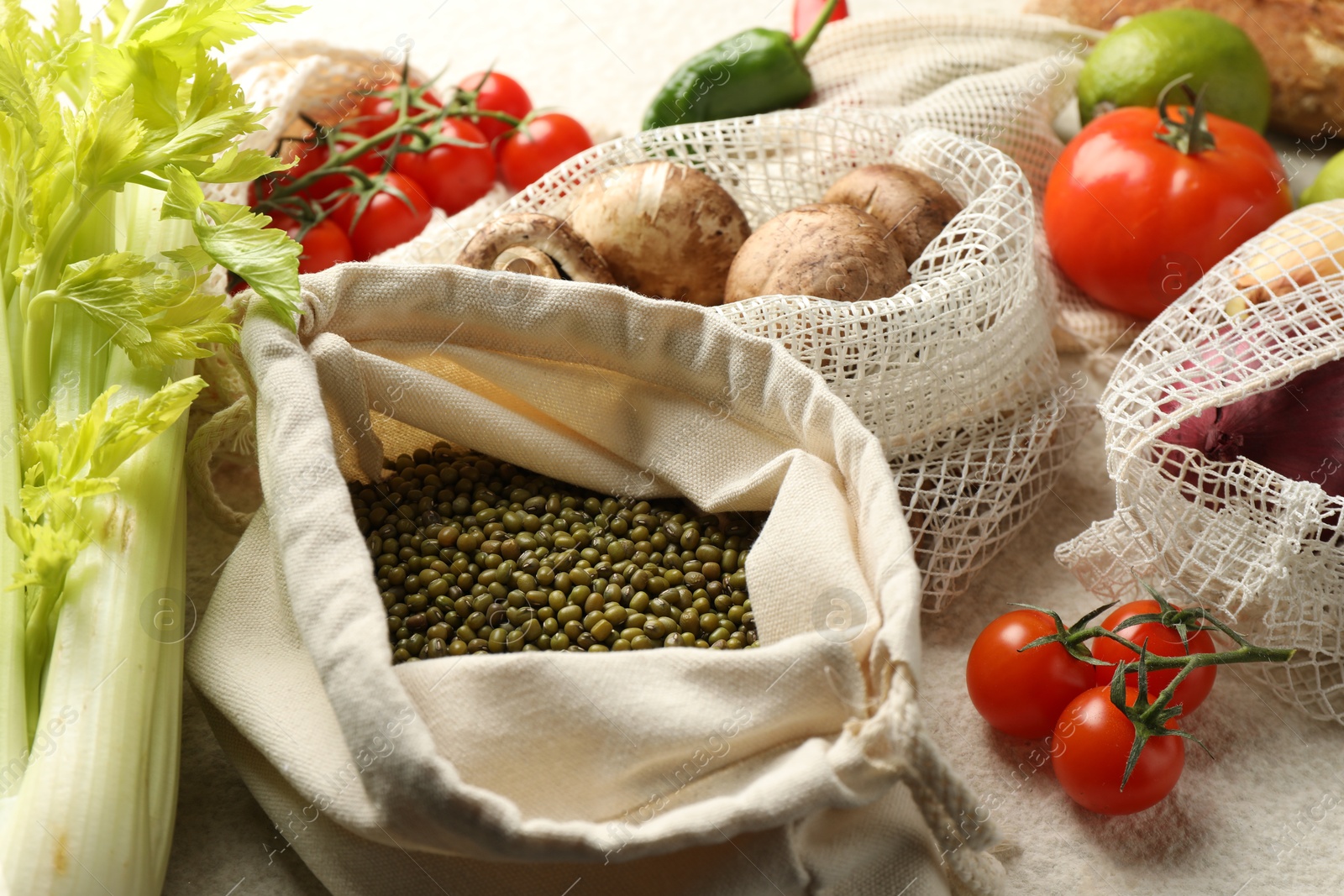 Photo of Eco bags with different food products on white textured table, closeup