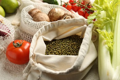 Photo of Eco bags with different food products on white textured table, closeup