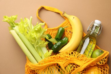 Photo of Eco bag with vegetables, fruits and bottle of drink on dark beige background, top view