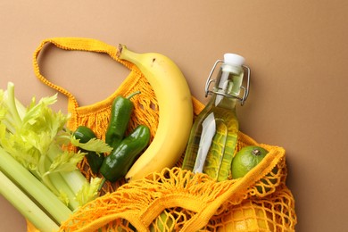 Photo of Eco bag with vegetables, fruits and bottle of drink on dark beige background, top view