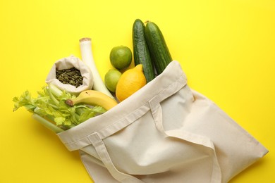 Photo of Eco bag with vegetables, fruits and pumpkin seeds on yellow background, top view